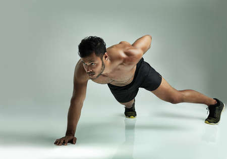 Youve got to push it. Studio shot of a young man doing a one hand pushup against a gray background.