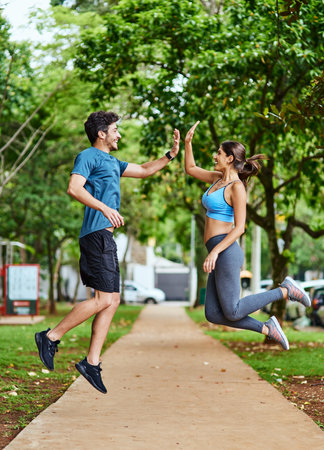 That workout was so worth it. Shot of a sporty young couple high fiving in mid-air while exercising outdoors.の写真素材