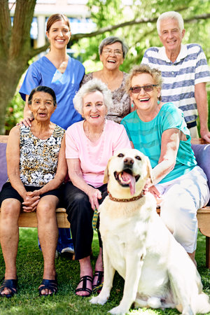 Their autumn years are filled with happiness. Portrait of a group of smiling seniors and a nurse outside with a labrador.の写真素材