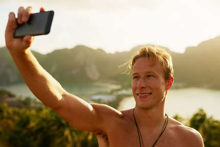 Wish you were here. Shot of a happy young man taking a selfie with his cellphone while on holiday.