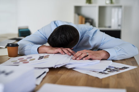 Its another overwhelming day in the office. Shot of a tired young businessman with his head down on...
