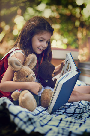 Enjoying storytime with her fluffiest little friends. Cropped shot of a little girl reading a book with her toys in the woods.の写真素材