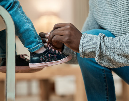 A dads job. Cropped shot of an unrecognizable man helping his daughter tie her shoelaces in the living room at home.の写真素材