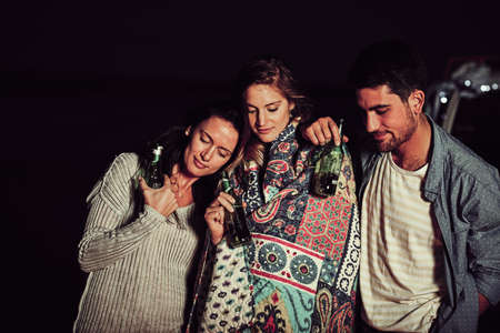 As close as can be. Cropped shot of a group of friends having a drink on the beach at night.