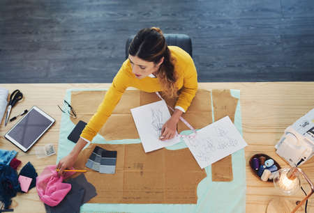 The desk of a designer. High angle shot of an attractive young fashion designer in her workshop.