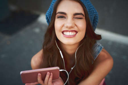 She found the right song for the occasion. Portrait of a carefree young woman seated on the floor while listening to music through her earphones outside during the day.の写真素材