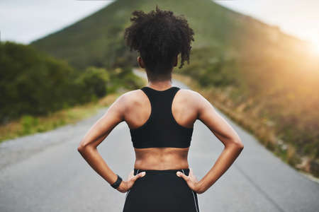 Time to get back on track. Rearview shot of an unrecognizable young sportswoman standing with her hands on her hips outside.の写真素材