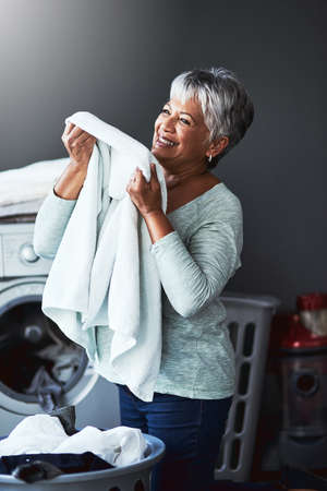 That smell of beautifully scented fabric softener. Shot of a mature woman smelling freshly washed towels while doing laundry at home.の写真素材