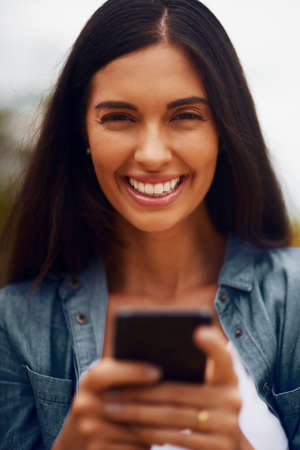 Its a great day to connect. Portrait of an attractive young woman using a mobile phone in a park.