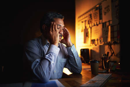 I cant deal with this now. Shot of a mature businessman looking stressed out while working late in...