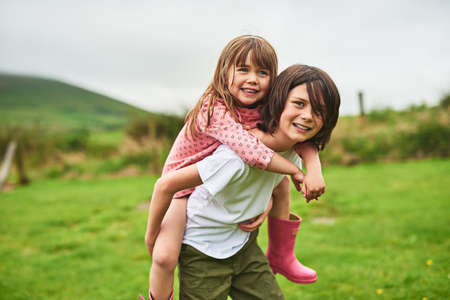 They have the most fun when they play together. Portrait of a little boy giving his sister a piggyback ride outdoors.の写真素材