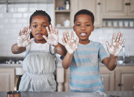 Dirty hands, pure hearts. Shot of a little girl and boy having fun while baking together at home.の写真素材