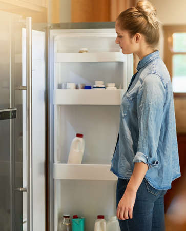 When hunger strikes.... Cropped shot of a young woman looking inside her fridge at home.の写真素材