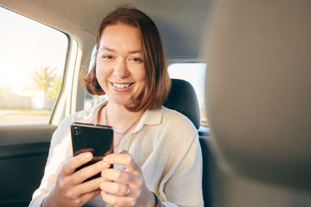 When life gives you wheels go see the world. Shot of a young woman using a smartphone while traveling in a car.の写真素材