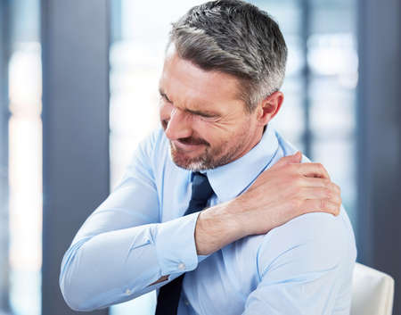 Backache is such a pain. Shot of a mature businessman suffering from backache at work.の写真素材