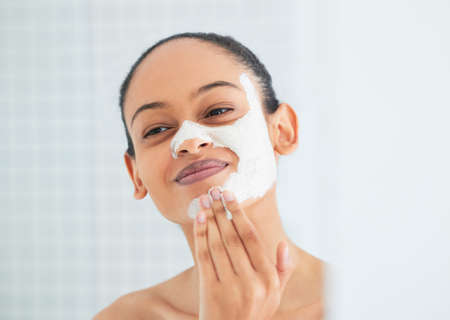 Some self-love was definitely needed. Shot of an attractive young woman standing alone in her bathroom at home and applying a face mask.の写真素材