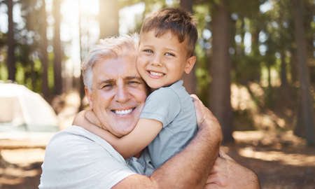 Hes my pride and joy. Cropped portrait of a handsome mature man and his grandfather hugging while camping in the woods.の写真素材