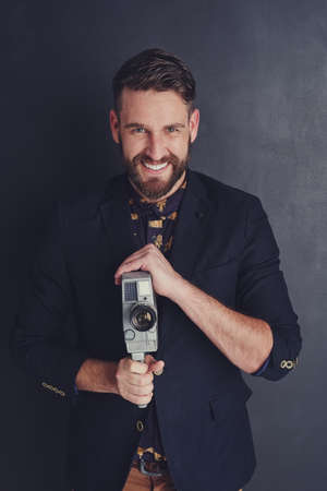 Smile, youre on candid camera. Portrait of a trendy young man with a vintage camera posing against a...