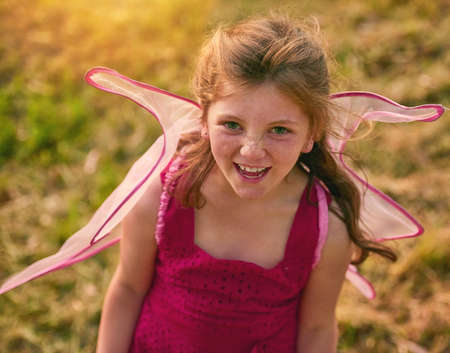 Pretty as a picture in pink. Portrait of a cute little girl looking up at the camera while playing in the park.の写真素材