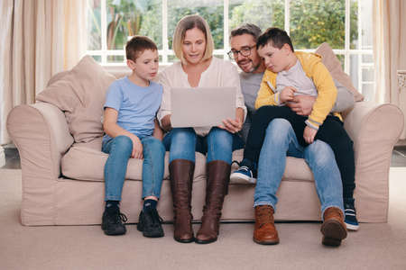 Whos getting the snacks. Shot of a young family bonding while using a laptop on the sofa together at...