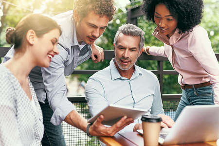 Working together is what makes them successful. Shot of a team of colleagues using a laptop and digital tablet together during a meeting outdoors.の写真素材