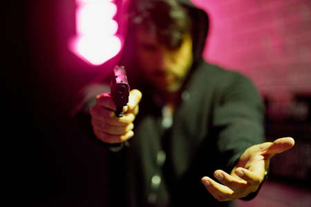 Crime is rife in all big cities. Portrait of a gun-wielding thief aiming his weapon.