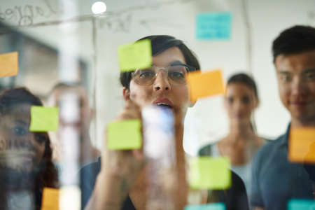 Planning is the first step. Cropped shot of a group of young designers planning on a glass board.の写真素材