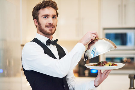 This is our speciality. Cropped portrait of a handsome young waiter holding a plate of food in a restaurant.の写真素材