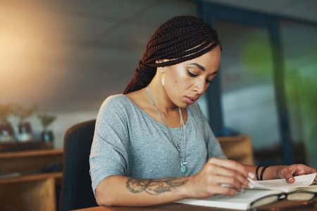 Taking a little break with her book. Cropped shot of a young woman reading a book while working late...