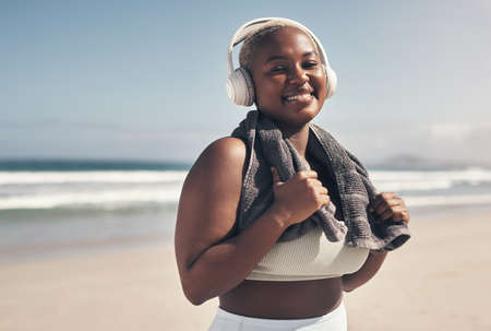 Im working on me, for me. Shot of a sporty young woman wearing headphones and a towel around her neck on the beach.の写真素材
