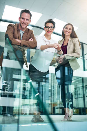 Were taking this company to the top. Portrait of a group of colleagues leaning on a railing together in a large modern office.の写真素材