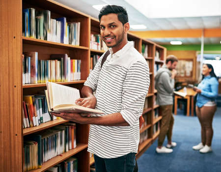 Put in the hard work for the good of your future. Portrait of a university student reading a book in the library at campus.の写真素材