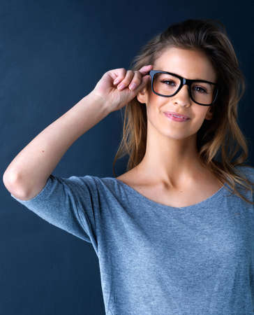 All the better to see with. Studio portrait of a cute teenage girl in glasses posing against a dark background.の写真素材