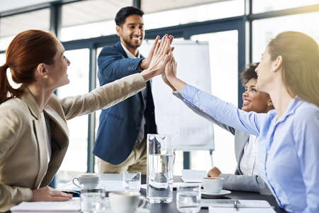 Everyones on board with this plan. Shot of a group of businesspeople high-fiving in the boardroom.の写真素材