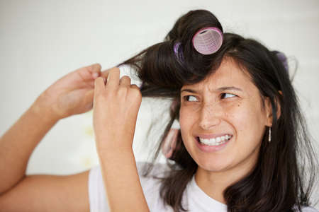 The things we do for a good hairdo. Shot of a young woman taking rollers out of her hair.の写真素材