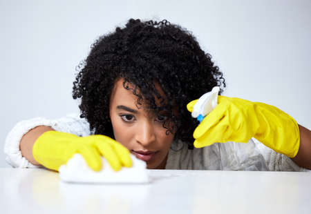 Be thorough when cleaning. Shot of a young woman spraying down a counter to clean it.