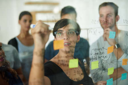 Planning is the first step. Cropped shot of a group of young designers planning on a glass board.の写真素材