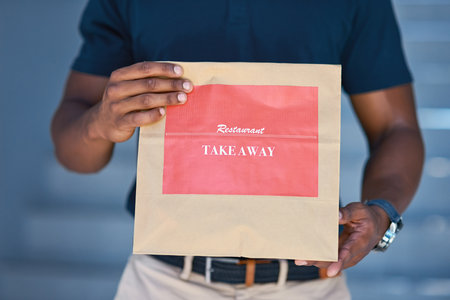 Delivered fresh and fast. Cropped shot of an unidentifiable delivery man holding a restaurant takeaway.の写真素材