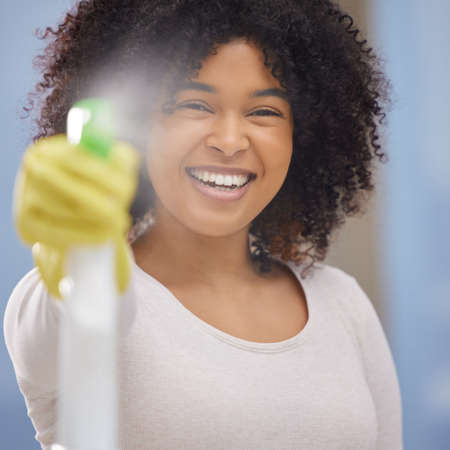 Goodbye fingerprints. Shot of an attractive young woman standing alone and spraying a bottle of detergent while doing the chores at home.の写真素材