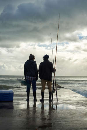 Its been a great day.... Full length shot of two young men fishing at the ocean in the early morning.の写真素材
