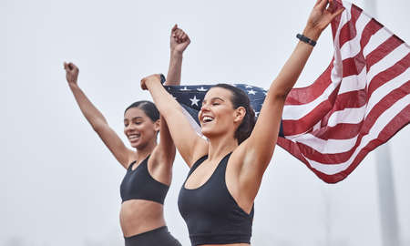 Women run the world. Shot of female athletes celebrating their win while holding a flag.の写真素材