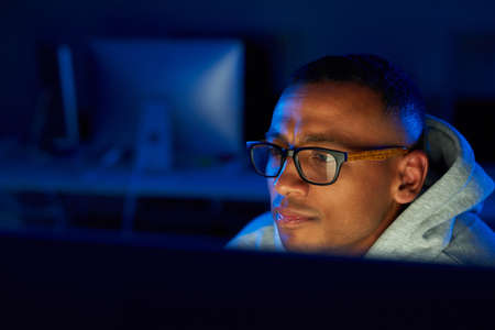 Taking a closer look at things. Shot of a young male hacker cracking a computer code in the dark.の写真素材