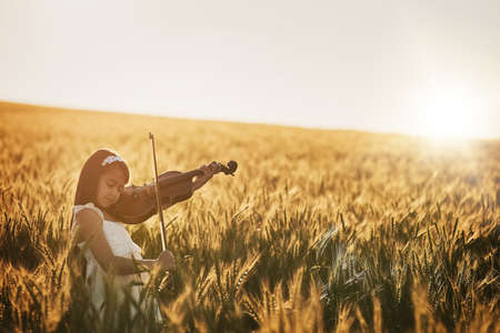 Giving the crops a little musical encouragement. Shot of a cute little girl playing the violin while...