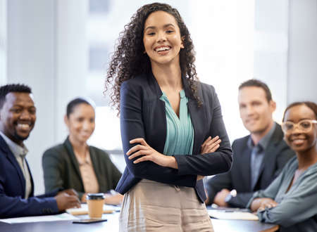 Me and my team. Cropped portrait of an attractive young businesswoman standing in the boardroom with her arms folded and her colleagues in the background.の写真素材