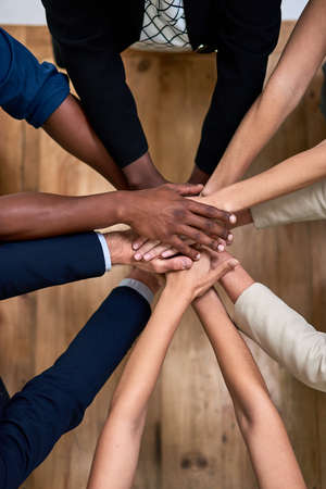Teamwork brings out our best. High angle shot of a group of unidentifiable businesspeople piling their hands in unity in the office.の写真素材
