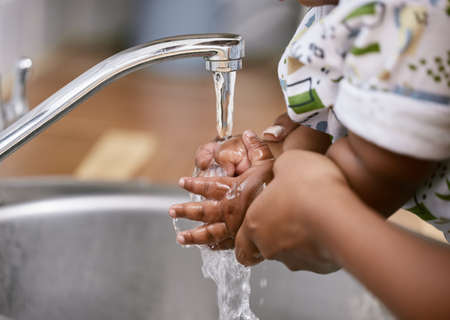 Keeping our hands clean. Shot of an unrecognizable child and parent washing their hands at home.の写真素材