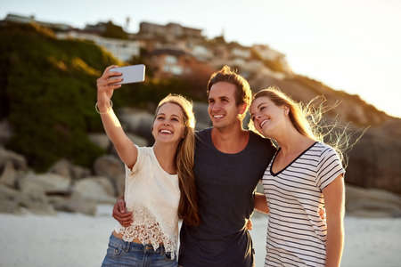 Selfies are digital memories. Shot of three friends taking a selfie at the beach.の写真素材