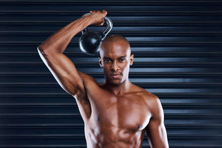 Are you truly committed. Shot of a sporty young man working out with weights as part of his exercise routine.の写真素材