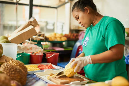 Only the best produce makes the cut. Shot of a woman slicing fruit in a Thai food market.