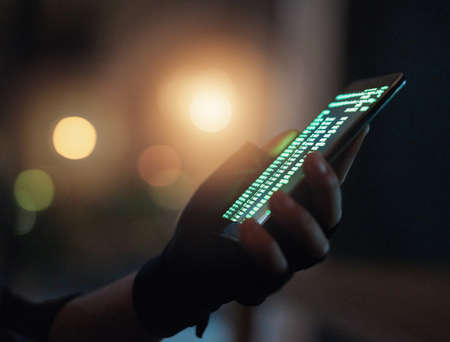 Protect yourself from fraudsters. Shot of an unrecognisable hacker using a cellphone in the dark.の写真素材